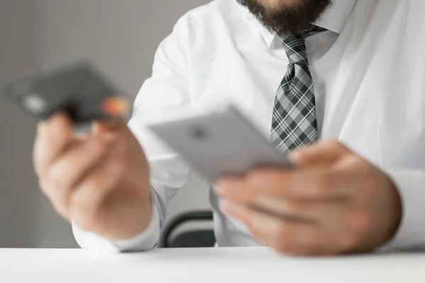 Joven hombre de negocios con una tarjeta de crédito bancaria en sus manos. Pagos en línea a través del teléfono. Pago de bienes en línea. Comercio en línea en el cambio de divisas. Smartphone e Internet Commerce . — Foto de Stock