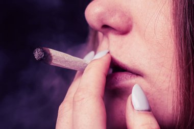 Esrar, elinde esrar Bir kadın sigara içiyor. Siyah arka planda sigara içmek. Tıbbi marihuana kullanımı ve esrar kullanımının yasallaştırılması kavramları. Siyah arka planda Pembe renklendirme