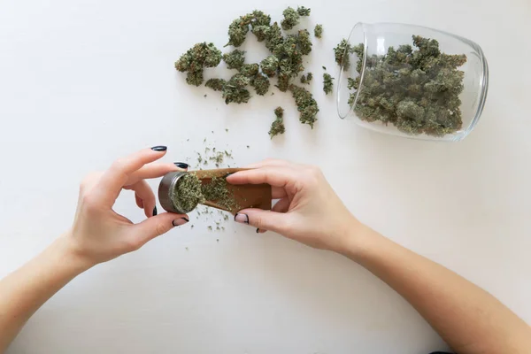 Woman preparing and rolling marijuana cannabis joint. Marijuana use concept. Woman rolling a marijuana joint on white background. Close up of marijuana blunt with grinder. Top view — Stock Photo, Image