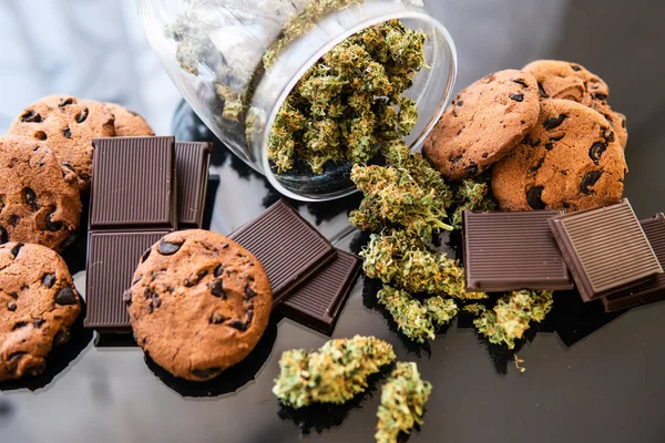 Behandeling van medicinale marihuana voor gebruik in voedsel, zwarte achtergrond. Chocolade en koekjes met cannabis en knoppen marihuana op tafel. Concept van koekjes en chocolade met cannabiskruid CBD. — Stockfoto