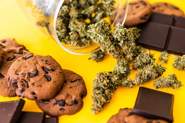 Sušenky a čokoládu s trávou a marihuanou na stole. Cannabis CBD bylinková čokoláda a sušenky. Léčba lékařské marihuany pro použití v potravinách, žluté pozadí. — Stock fotografie