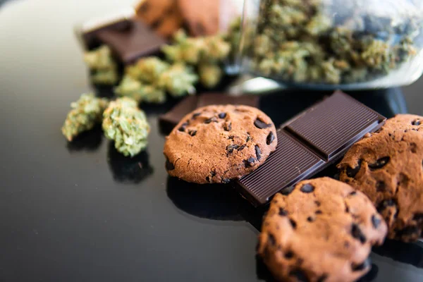 Chocolate e biscoitos com maconha e botões de maconha na mesa. Conceito de Cookies e chocolate com erva de cannabis CBD. Tratamento de maconha medicinal para uso em alimentos, fundo preto . — Fotografia de Stock