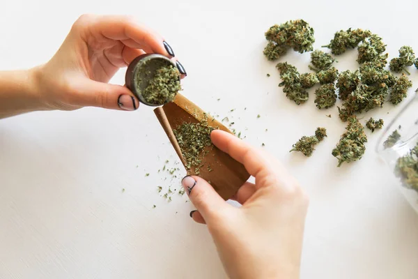 Cierre de marihuana roma con molinillo. Concepto de consumo de marihuana. Mujer rodando un porro de marihuana sobre fondo blanco. Mujer preparando y rodando marihuana marihuana conjunta . — Foto de Stock