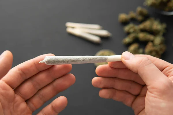 Joint mit Unkraut in der Hand, Cannabis-Knospen auf schwarzem Tisch, Nahaufnahme, Mühle mit frischem Marihuana, — Stockfoto