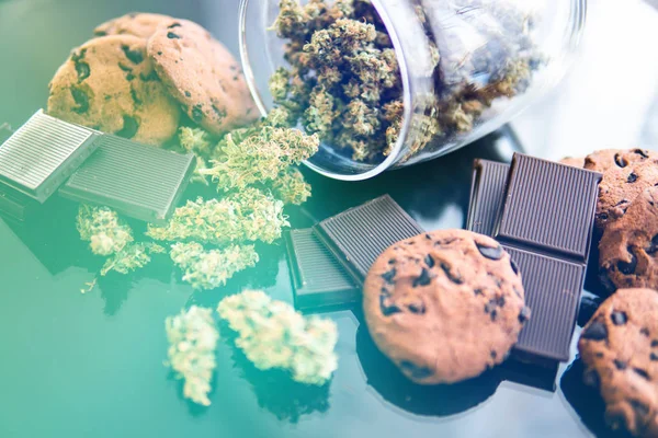 Cioccolato e biscotti con cannabis e germogli di marijuana sul tavolo. Trattamento della marijuana medica per uso alimentare, sfondo nero. Concetto di biscotti e cioccolato con erba di cannabis CBD . — Foto Stock