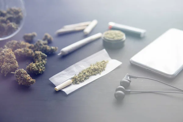 Boutons de marijuana sur la table noire, gros plan, broyeur à la main avec du cannabis frais, joint avec de l'herbe, fuites de lumière tons de couleur — Photo