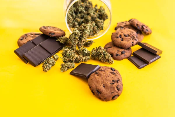 Cannabis CBD erba Cioccolato e biscotti. Biscotti e cioccolato con cannabis e boccioli di marijuana sul tavolo. Trattamento della marijuana medica per uso alimentare, fondo giallo . — Foto Stock