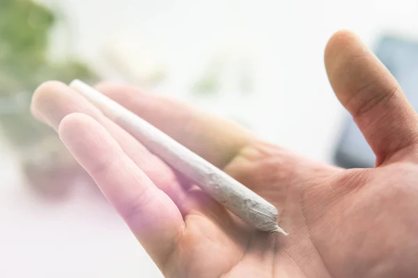 Joint met marihuana in de hand onkruid, close-up, Cannabis knoppen op witte tafel achtergrond, lichte lekken kleur tonen — Stockfoto