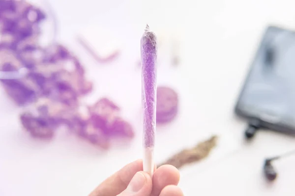Brotes de cannabis sobre fondo de mesa blanco, articulación con marihuana hierba en la mano, de cerca, fugas de luz tonos de color — Foto de Stock
