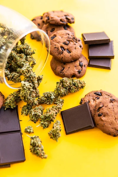 Léčba lékařské marihuany pro použití v potravinách, žluté pozadí. Sušenky a čokoládu s trávou a marihuanou na stole. Konopí CBD bylinková čokoláda a sušenky. — Stock fotografie
