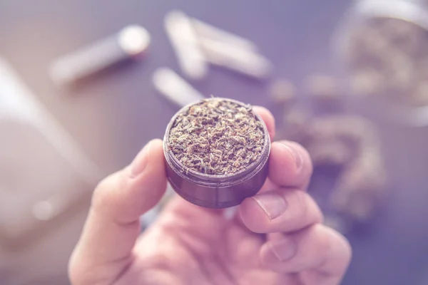 Grinder in de hand met verse cannabis, marihuana knoppen op zwarte tafel, onkruid voor gezamenlijke, close-up, licht lekken kleur tonen — Stockfoto