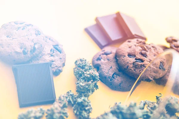 Cannabis CBD erva Chocolate e bolachas. Biscoitos e Chocolate com erva daninha e botões de maconha na mesa. Tratamento de maconha medicinal para uso em alimentos, fundo amarelo. fugas de luz — Fotografia de Stock