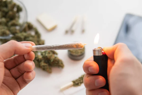 Junção com maconha com isqueiro na mão, erva daninha, botões de Cannabis na mesa branca, close-up , — Fotografia de Stock