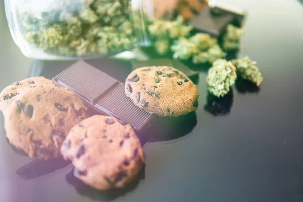 Chocolate e biscoitos com maconha e botões de maconha na mesa. Conceito de Cookies e chocolate com erva de cannabis CBD. Tratamento de maconha medicinal para uso em alimentos, fundo preto . — Fotografia de Stock