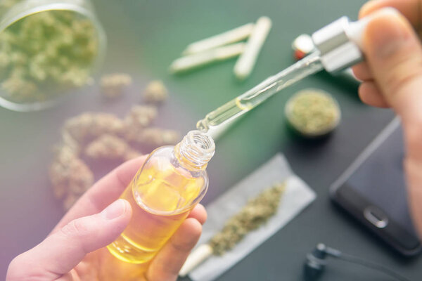 medical marijuana concept, Hand holding bottle of Cannabis oil in pipette, natural herb, CBD cannabis OIL. hemp product, close up, light leaks color tones