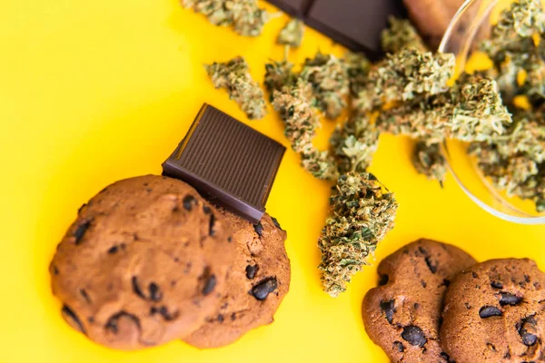 Biscoitos e Chocolate com erva daninha e botões de maconha na mesa. Cannabis CBD erva Chocolate e bolachas. Tratamento de maconha medicinal para uso em alimentos, fundo amarelo . — Fotografia de Stock