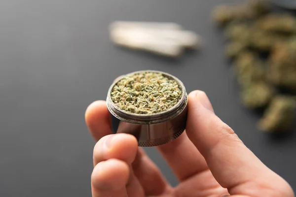 in hand grinder with fresh marijuana, close up, Cannabis buds on black table, joint with weed,