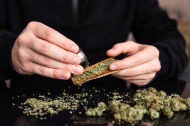 Esrarkeşin çakmakla esrar içtiği yeri kapatın. Marihuana hazırlayan ve yuvarlayan adam. Esrar saran bir adam.