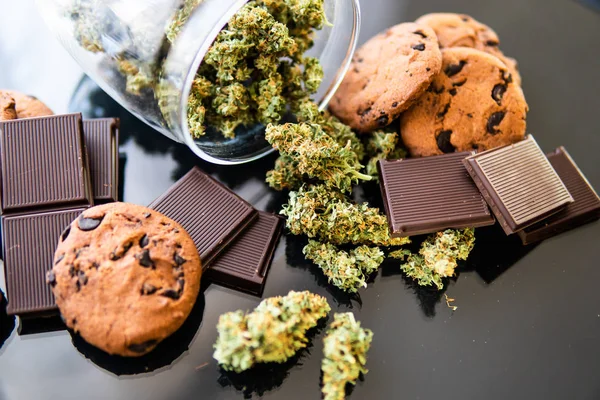 Chocolate e biscoitos com maconha e botões de maconha na mesa. Conceito de Cookies e chocolate com erva de cannabis CBD. Tratamento de maconha medicinal para uso em alimentos, fundo preto . — Fotografia de Stock