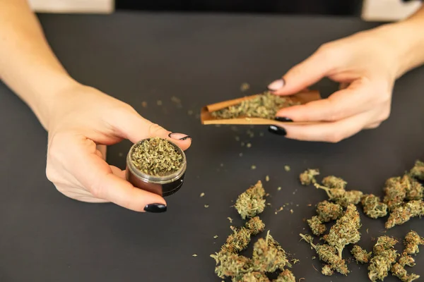 Woman rolling a marijuana joint. Woman preparing and rolling marijuana cannabis joint. Close up of marijuana blunt with grinder. Marijuana use concept. — ストック写真