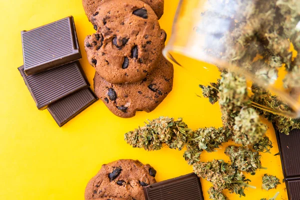 Tratamento da maconha medicinal para uso em alimentos, fundo amarelo. Cookies e chocolate com cannabis e botões de maconha na mesa. Cannabis CBD ervas Chocolate e biscoitos. — Fotografia de Stock