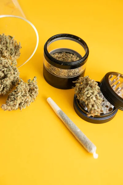 Indica medical health. Yellow background. The pot leaves on buds. Cannabis nature bud. Sativa THC CBD. Marijuana weed bud and grinder. Joint weed. Vertical shot .