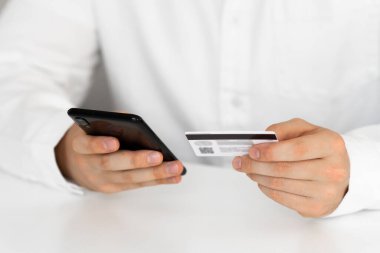 Kredi kartıyla internet alımı ve geçmişi bulanık bir şekilde evde oturan akıllı bir telefon. Kredi kartı tutan ellerini kapat ve cep telefonu kullan, online alışveriş, adam mutlu..