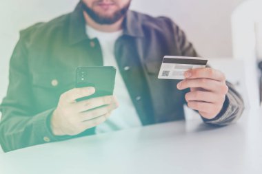 İnternetten alışveriş için el kredi kartı. İnternet alışverişi. Ödeme internet üzerinden akıllı telefon işyerinde. Kredi kartıyla internet alımı ve geçmişi bulanık bir şekilde evde oturan akıllı bir telefon..