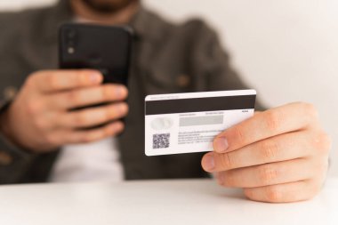 Ödeme internet üzerinden akıllı telefon işyerinde. İnternetten alışveriş için el kredi kartı. İnternet alışverişi. Kredi kartıyla internet alımı ve geçmişi bulanık bir şekilde evde oturan akıllı bir telefon..