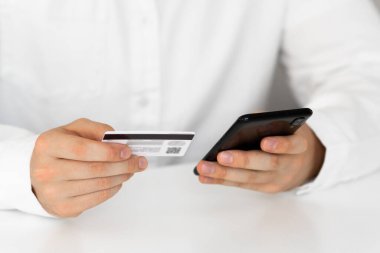 Kredi kartıyla internet alımı ve geçmişi bulanık bir şekilde evde oturan akıllı bir telefon. Kredi kartı tutan ellerini kapat ve cep telefonu kullan, online alışveriş, adam mutlu..