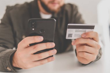 İnternetten alışveriş için el kredi kartı. İnternet alışverişi. Kredi kartıyla internet alımı ve geçmişi bulanık bir şekilde evde oturan akıllı bir telefon. İş yerinde online alışveriş akıllı telefonu ödemesi.