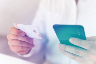 Akıllı telefon kullanan ve sosyal ödemeli online akıllı telefondan iş yerinde kredi kartı tutan bir adam. Çevrimiçi alışveriş konseptini sabah ışığında yapan genç adamın yakınlaşması.