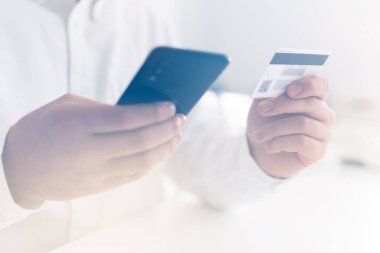 Online alışveriş için akıllı telefon kullanıyor. Çevrimiçi ödeme, kredi kartı ve akıllı telefon kullanan ve sosyal online alışveriş konsepti sabah ışığında kredi kartı tutan İşadamı elleri.