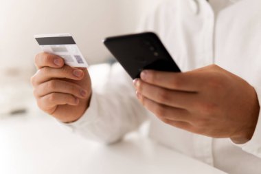 Online alışveriş için akıllı telefon kullanıyor. Akıllı telefon ve içinde sosyal online alışveriş konsepti olan kredi kartı sabah ışığında tutuluyor. Çevrimiçi ödeme, kredi kartı ve iş adamlarının elleri