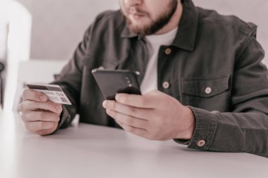 Sabah ışığında üzerinde sosyal online alışveriş konsepti olan kredi kartı taşıyor. Kredi kartı tutan ellerini kapat ve akıllı cep telefonu kullan. Akıllı telefon kullanan iş adamı elleri ve...