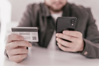 Kredi kartıyla internet alımı ve geçmişi bulanık bir şekilde evde oturan akıllı bir telefon. İnternetten alışveriş için el kredi kartı. İnternet alışverişi. İş yerinde online alışveriş akıllı telefonu ödemesi.