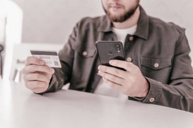İnternetten alışveriş için el kredi kartı. İnternet alışverişi. Ödeme internet üzerinden akıllı telefon işyerinde. Kredi kartıyla internet alımı ve geçmişi bulanık bir şekilde evde oturan akıllı bir telefon..