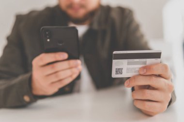 Ödeme internet üzerinden akıllı telefon işyerinde. İnternetten alışveriş için el kredi kartı. İnternet alışverişi. Kredi kartıyla internet alımı ve geçmişi bulanık bir şekilde evde oturan akıllı bir telefon..