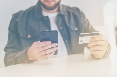 İnternetten alışveriş yapmak için kredi kartı. İnternet alışverişi. İş yerinde internet üzerinden akıllı telefon alışverişi. Kredi kartıyla internet alımı ve geçmişi bulanık bir şekilde evde oturan akıllı bir telefon..