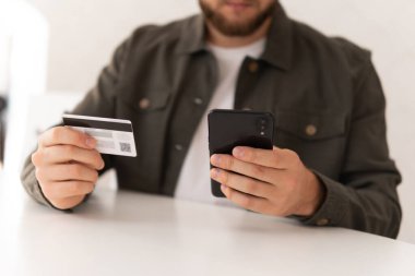 Kredi kartıyla internet alımı ve geçmişi bulanık bir şekilde evde oturan akıllı bir telefon. İnternetten alışveriş yapmak için kredi kartı. İnternet alışverişi. İş yerinde CPayment çevrimiçi alışveriş akıllı telefonu.