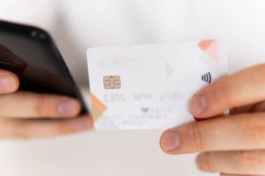 İş yerinde ödemeli online akıllı telefon. Akıllı telefon kullanan ve sosyal online alışveriş konseptiyle kredi kartı tutan genç bir adamın el ele tutuşması..