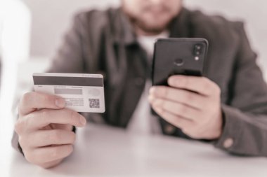 İnternetten alışveriş için el kredi kartı. İnternet alışverişi. Ödeme internet üzerinden akıllı telefon işyerinde. Kredi kartıyla internet alımı ve geçmişi bulanık bir şekilde evde oturan akıllı bir telefon..