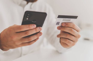 İnternet üzerinden alışveriş yapmak için kredi kartı tutan bir adamın elleri. Çevrimiçi ödeme, iş yerinde Ödeme yapan genç adamın çevrimiçi akıllı telefonu. Web alışverişi .