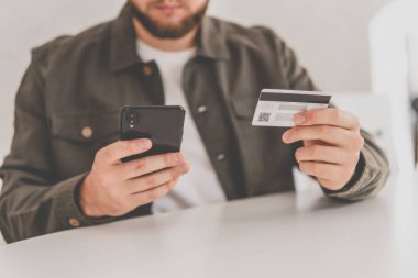 Ödeme internet üzerinden akıllı telefon işyerinde. Kredi kartıyla internet alımı ve geçmişi bulanık bir şekilde evde oturan akıllı bir telefon. İnternetten alışveriş için el kredi kartı. Web alışverişi .