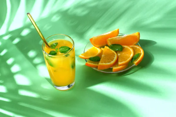 Orange juice with palm leaves on green