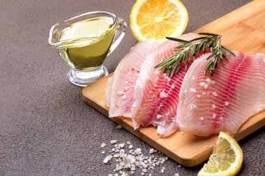 Kesme tahtası üzerinde limon, biberiye ve marul ile Tilapia fileto.