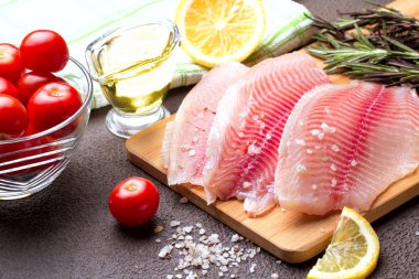 Kesme tahtası üzerinde limon, biberiye ve marul ile Tilapia fileto.