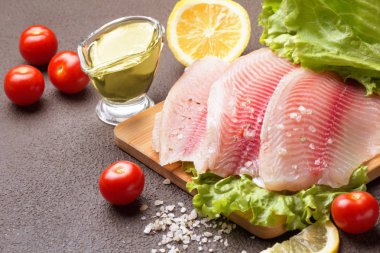 Kesme tahtası üzerinde limon, biberiye ve marul ile Tilapia fileto.