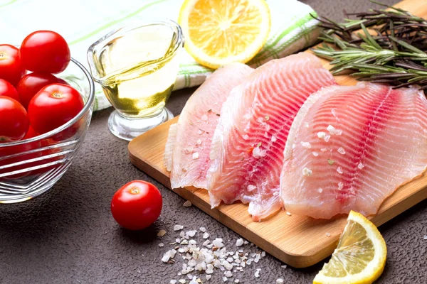 Kesme tahtası üzerinde limon, biberiye ve marul ile Tilapia fileto.