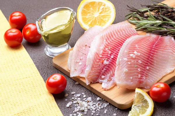 Kesme tahtası üzerinde limon, biberiye ve marul ile Tilapia fileto.